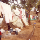 J. (Male, 23Yrs Old, Mathare IDP Camp, Kenya), Clothes hanged in the camp and a child staring at the photographer